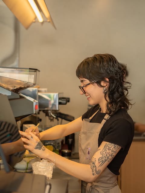 Barista de hema con delantal y tatuajes preparando una bebida